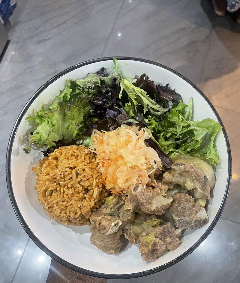A home-cooked jollof rice bowl with goat meat, sauerkraut and salad greens